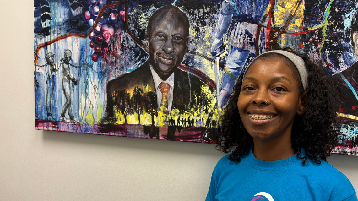 A woman standing in front of a painting of her grandfather.