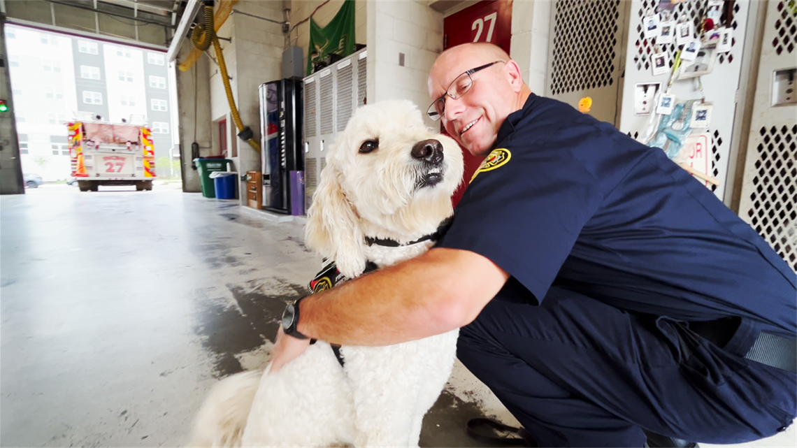 Firefighter Matt Waitrowski hugs Therapy Dog Phoenix, a white Goldendoodle, in Firehouse 27