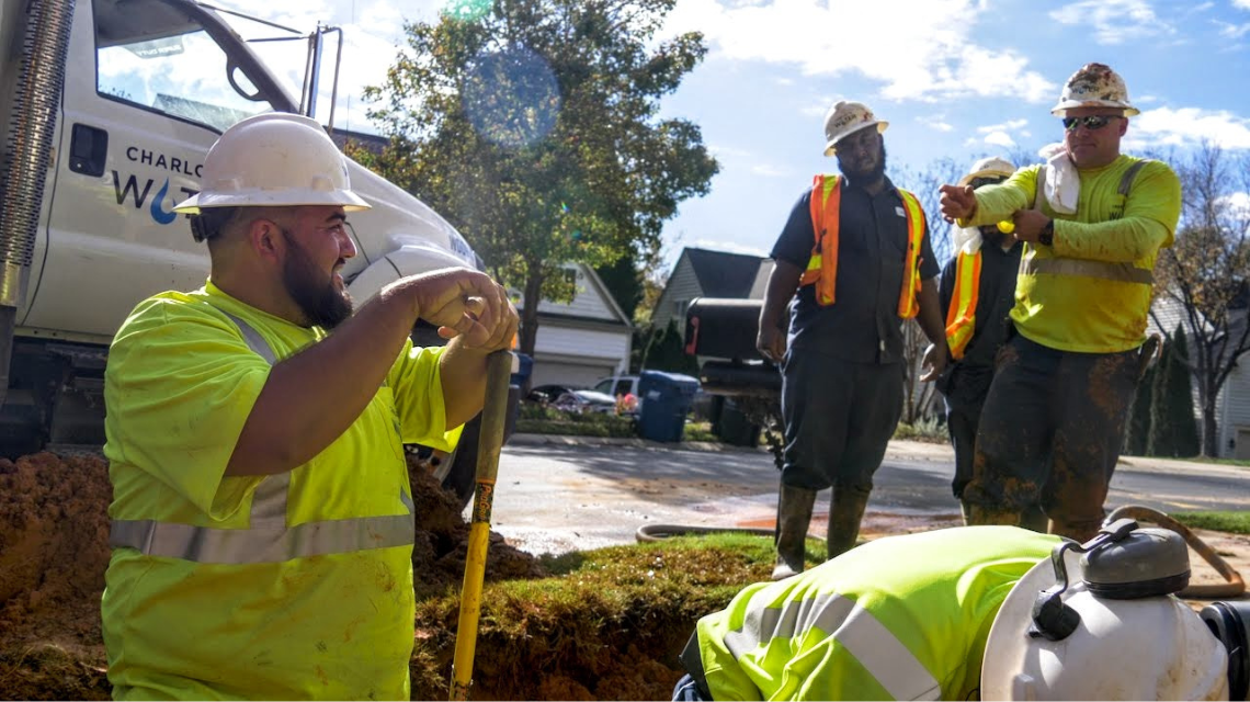 Charlotte Water workers in safety vests digging into the ground in front of a Charlotte Water truck.