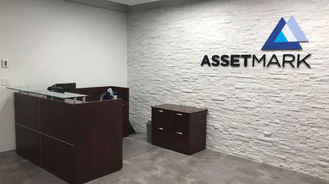 Interior of AssetMark office with logo on back wall and brown desk in front of it.