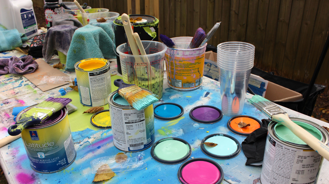 Open cans of paint and paint-covered brushes spead out on a table during a mural installation.