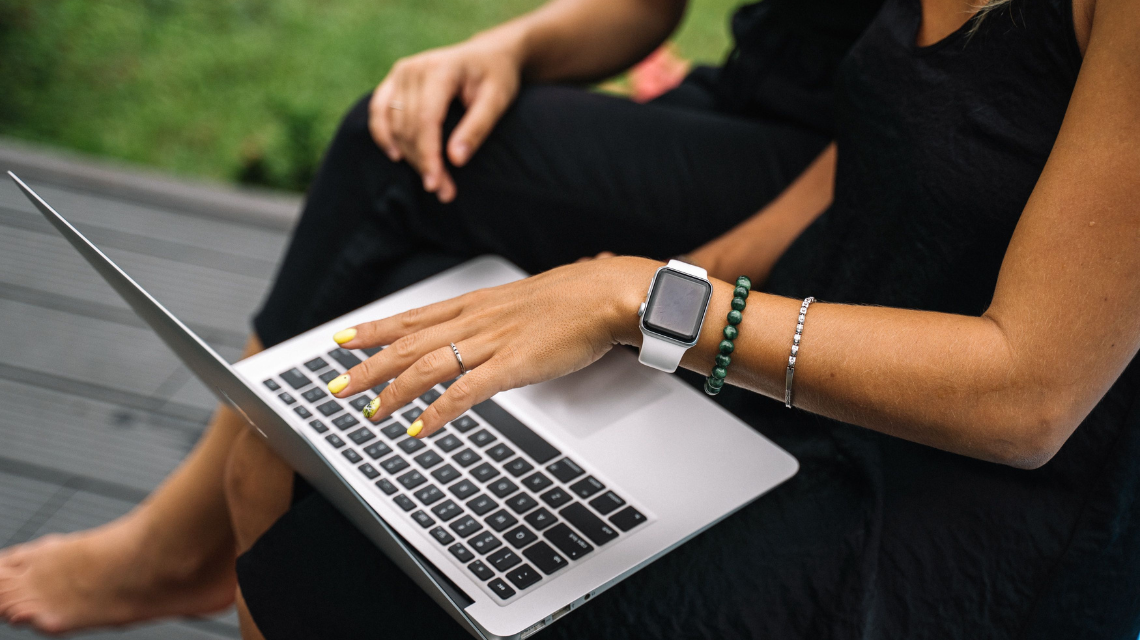 A woman wearing black interacts with a laptop next to a friend, also in black. Only their arms and legs are visible.
