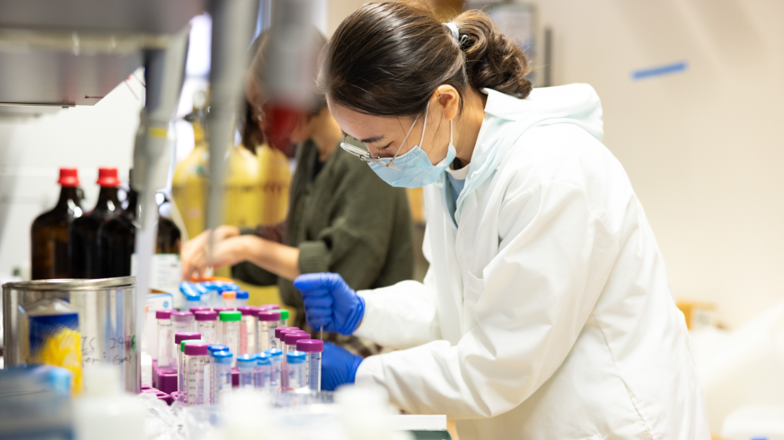 A woman works in a lab wearing a white coat.