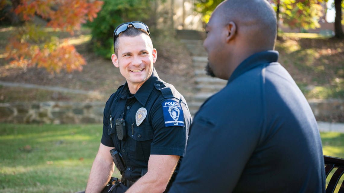 A CMPD officer sits with a resident in a public park.