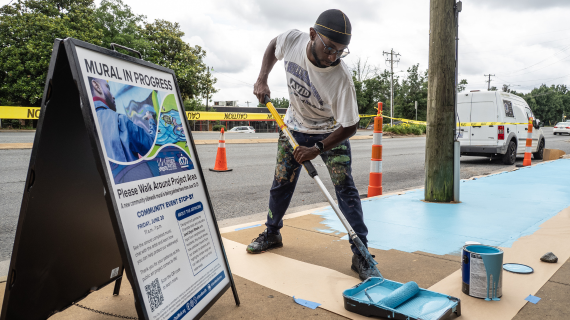 Jamil Dyair Steele begins a sidewalk mural outside of the Rosa Parks Place Community Transit Center.