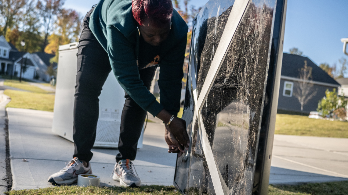 A woman tapes the glass side of a TV in the shape of an X before setting it on her curb for pickup.