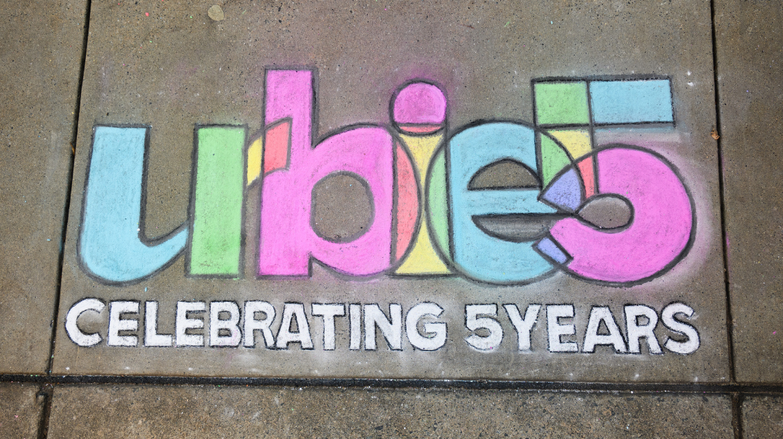 Urbies five-year logo written on a sidewalk in colorful chalk.