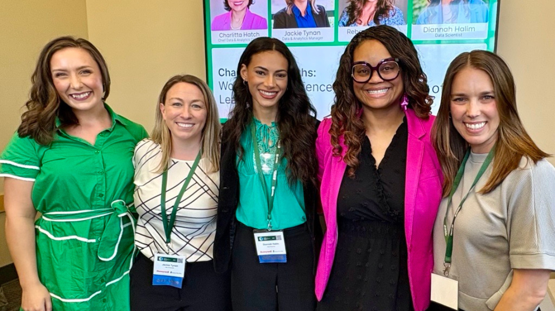 Five women pose together for a photo at a conference, where they presented.