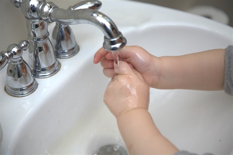 A child washes their hands in a sink with running water.